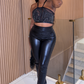 Woman in black sequin top and high-waisted black pants standing indoors.Model wearing Envy black metallic two-piece set with halter crop top and flared slit pants
